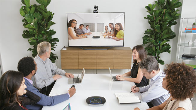 ビデオ会議を通して、会議室内で別のグループと会議をしているグループの写真